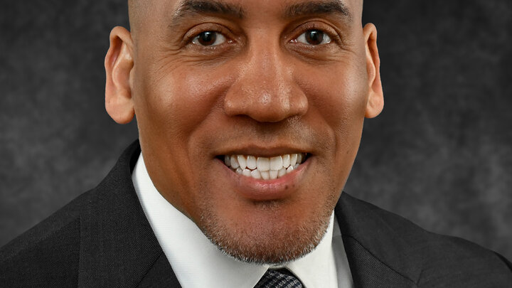 Man in a suit and tie smiling against a dark gray background.